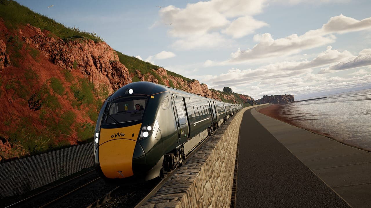 A dark green GWR express train running beside the sea beneath red cliffs in Train Sim World