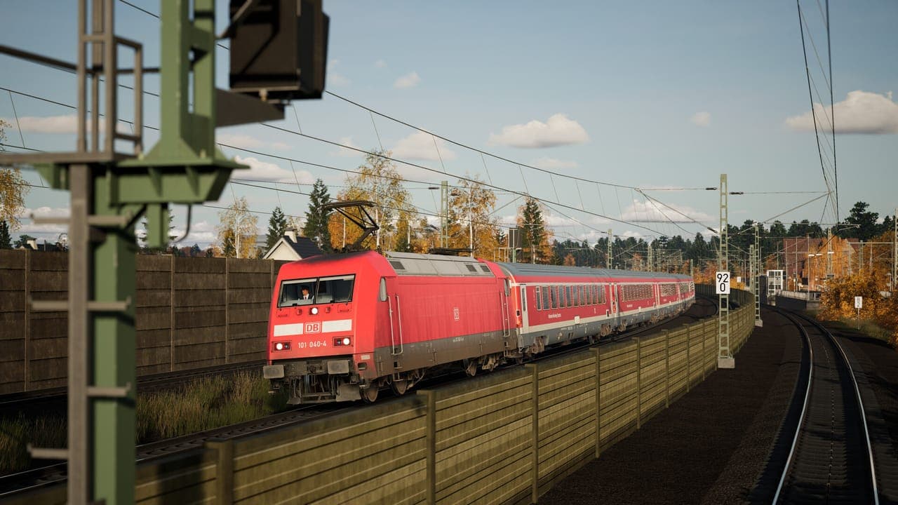 A red DB electric locomotive hauling red passenger coaches past a trackside noise barrier in Train Sim World