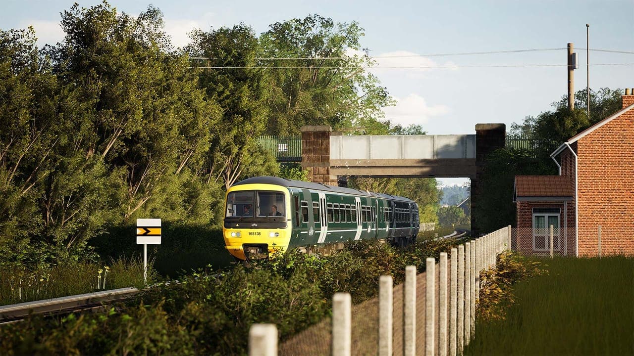 A green and yellow GWR Class 165 diesel unit coming under a road bridge between thick trees and a brick house in Train Sim World